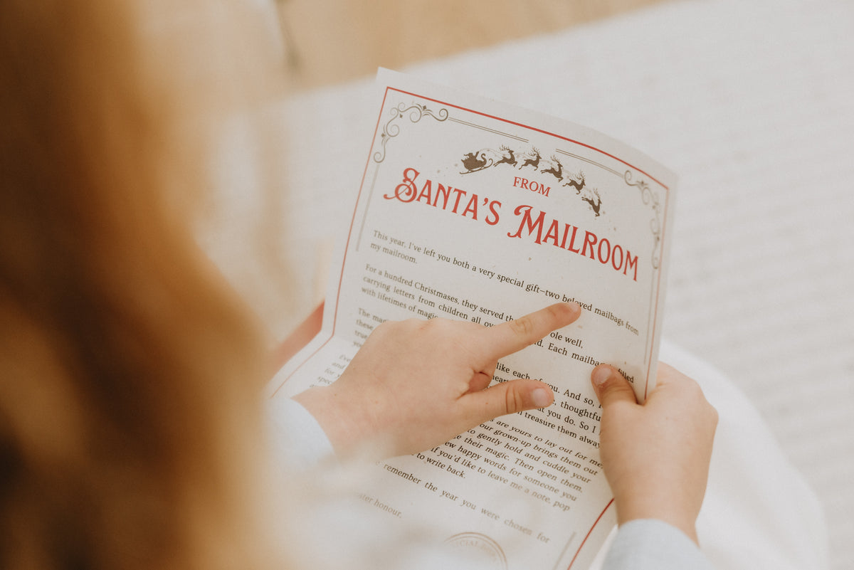 A person holding a printed card or letter titled "Santa's Mailroom" with both hands pointing at the text. 