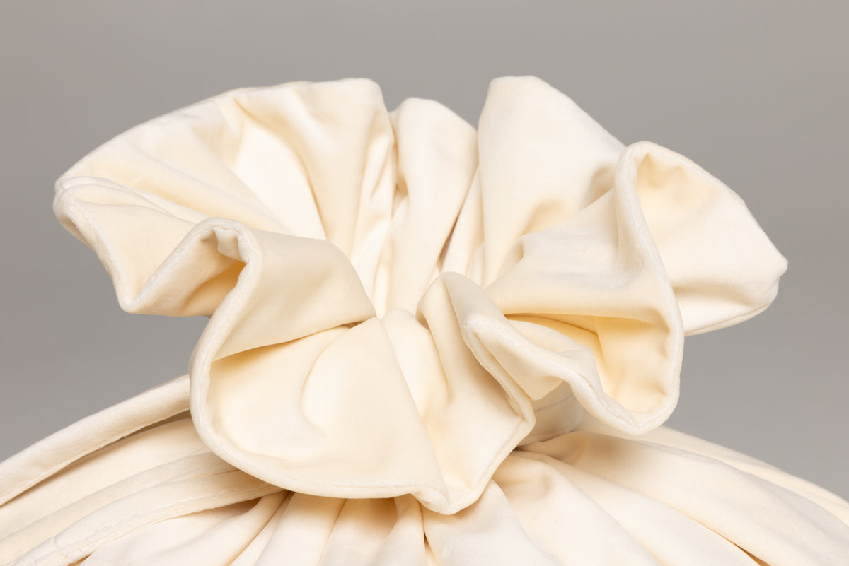 A close-up of a gathered cream-colored fabric accessory, likely a hair scrunchie or decorative fabric bow, showing soft folds and texture 