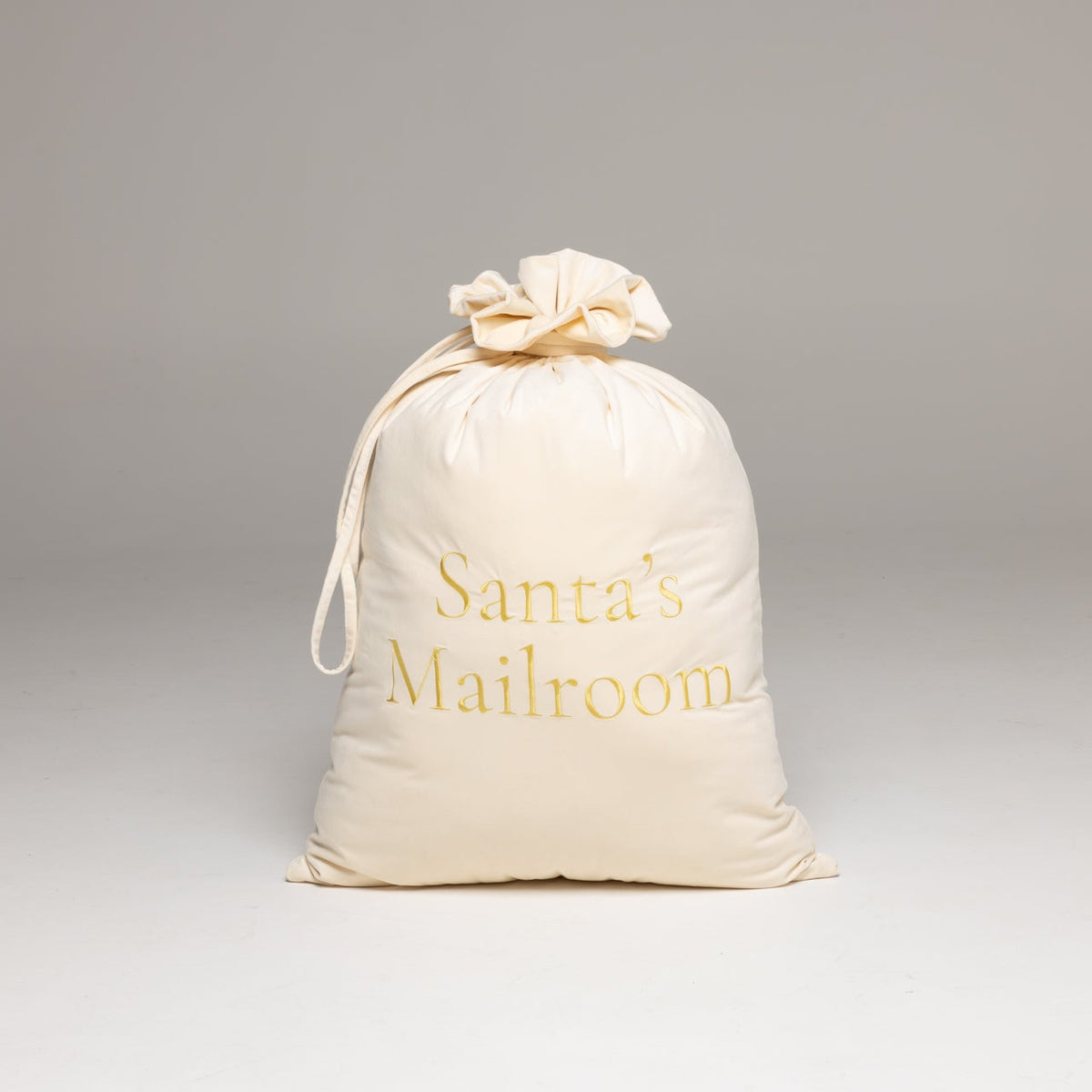 An off-white fabric drawstring sack with 'Santa's Mailroom' printed in gold lettering, 